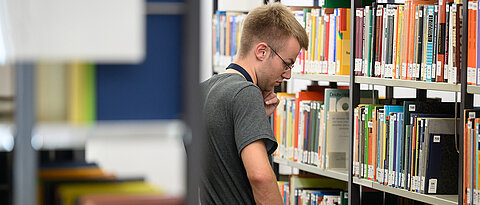 Man standing in a library (photo: University of Würzburg)