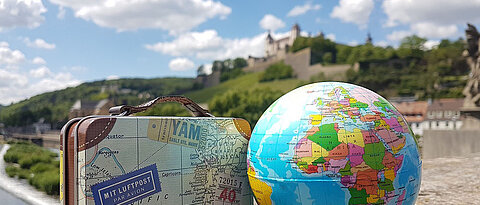 A suitcase and a globe with Marienberg castle in the background (photo: Faculty of Human Sciences)